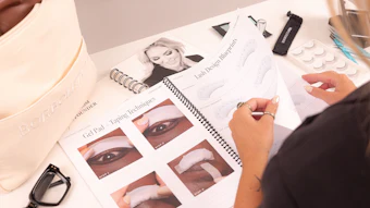 Beauty professional reviewing eye makeup application techniques with cosmetic products and instructional diagrams on workspace