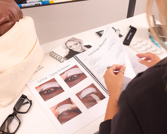 Beauty professional reviewing eye makeup application techniques with cosmetic products and instructional diagrams on workspace