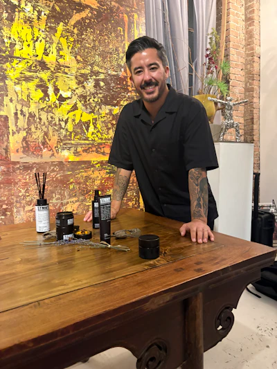 Man smiling at wooden table with STIMD branded product bottles and accessories in modern studio setting