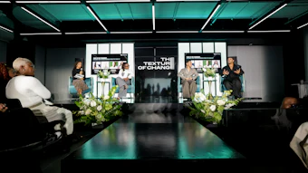 Professional panel discussion event with speakers seated on stage under teal lighting, featuring 'The Texture of Change' backdrop and white floral arrangements.