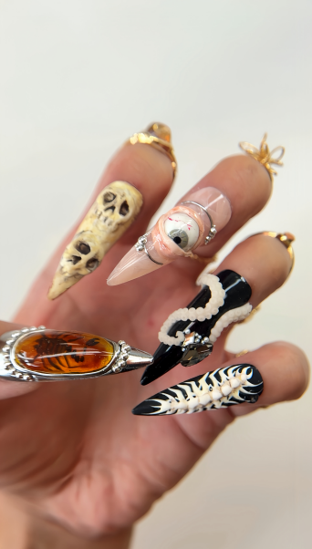 Hand displaying Halloween-themed nail art with skull, eye, and zebra stripe designs in gold, black, and white