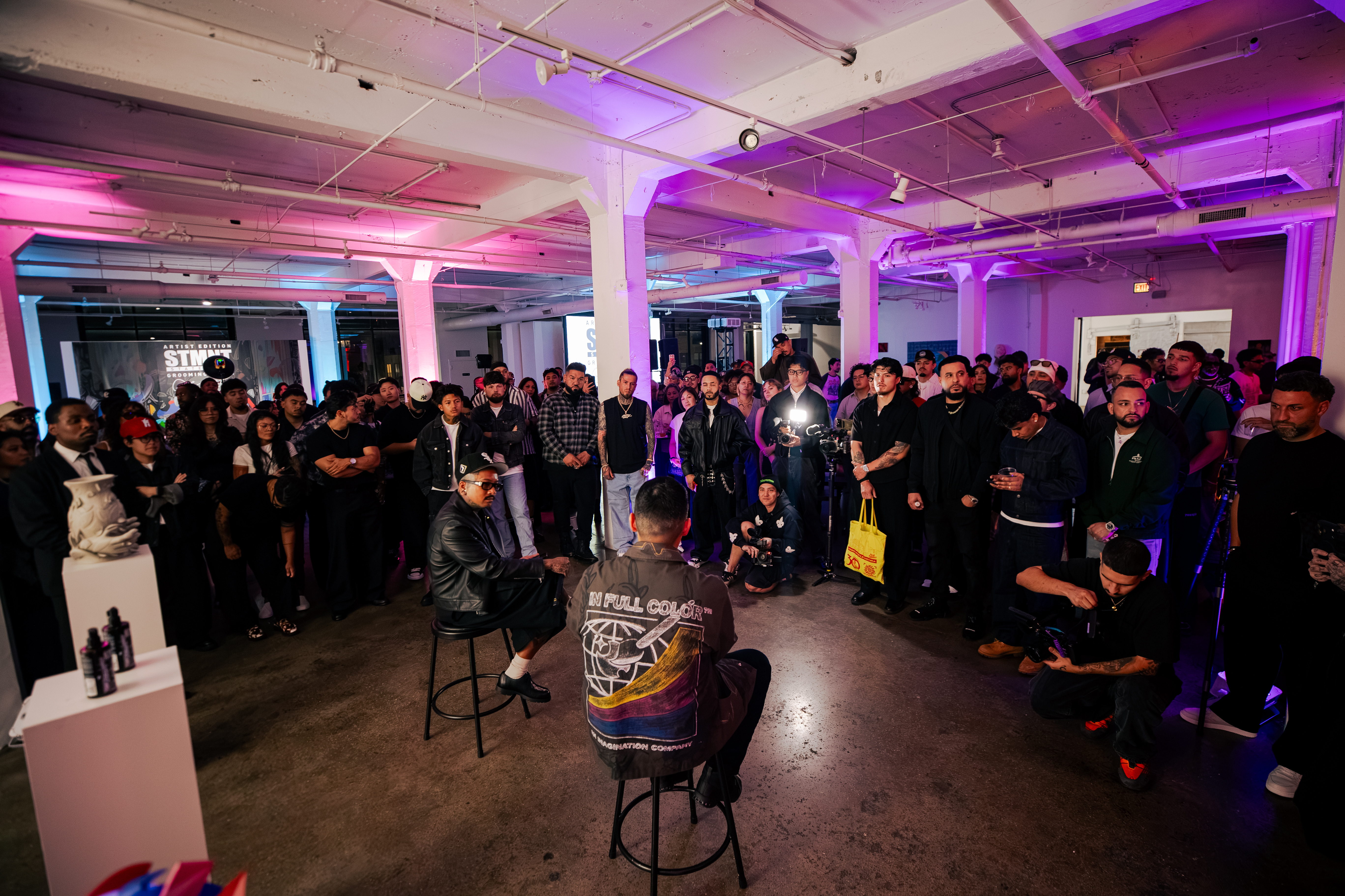 Large crowd of people gathered in a modern industrial venue with purple and pink ambient lighting during an event.