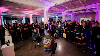 Large crowd of people gathered in a modern industrial venue with purple and pink ambient lighting during an event.