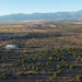 Aerial view of agricultural landscape with scattered trees, cultivated fields, and mountains under clear blue sky